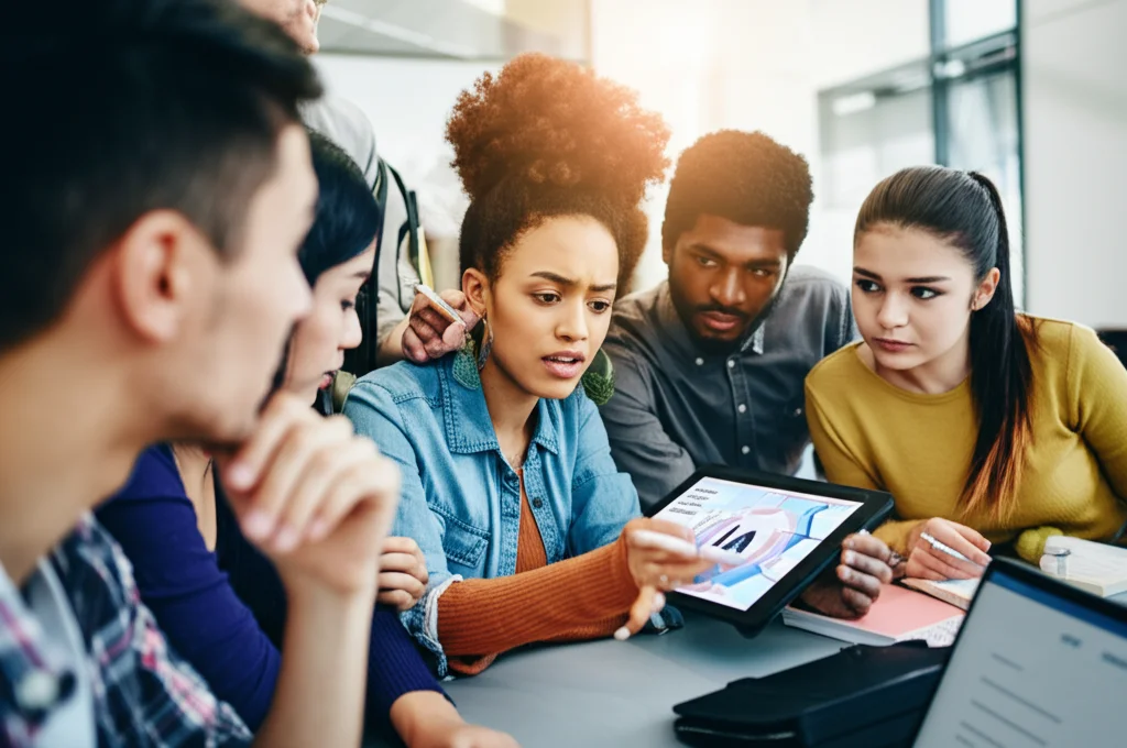 Un gruppo diversificato di giovani studenti di lingue, futuri insegnanti, in un'aula moderna e luminosa, discutono animatamente attorno a un tablet che mostra un'applicazione di IA per l'apprendimento linguistico. Alcuni sembrano curiosi, altri leggermente ansiosi. Fotografia di ritratto, obiettivo 35mm, profondità di campo per mettere a fuoco il gruppo centrale, illuminazione naturale controllata.