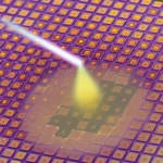 Macro fotografia di una metasuperficie high-tech con pattern geometrici di anelli quadrati concentrici di biossido di vanadio (VO2) su un substrato di silicio e oro. Un fascio di luce Terahertz stilizzato interagisce con la superficie. Obiettivo macro 100mm, illuminazione controllata per evidenziare i dettagli high-tech, alta definizione, mostrando la transizione di fase del materiale con un leggero effetto di cambiamento colore/riflettività su alcune aree.