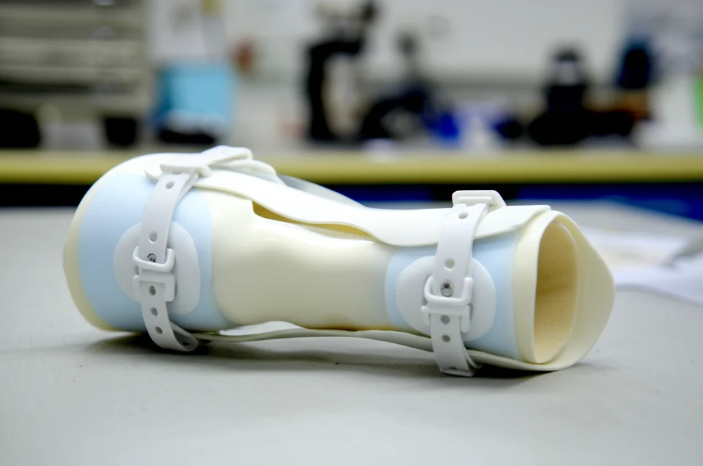 Primo piano di un tutore AFO in polipropilene bianco appoggiato su un tavolo da laboratorio, lente macro 90mm, illuminazione controllata, alta definizione, focus preciso sul materiale e sulla forma del tutore.