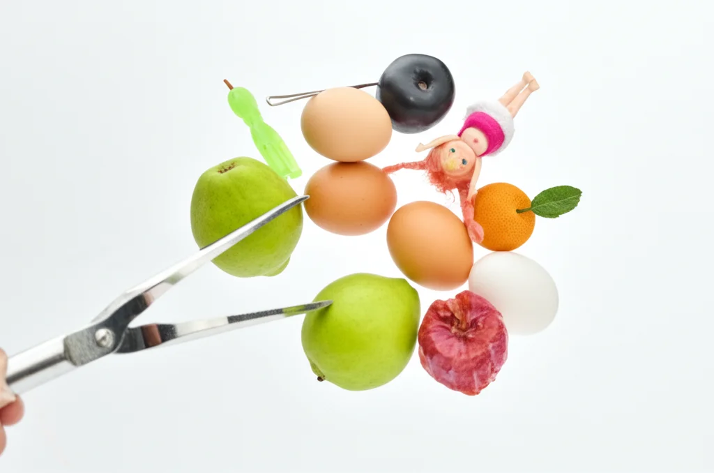 Scatto grandangolare, lente da 24 mm, che mostra la pinza frattale circondata da una varietà di oggetti che ha afferrato con successo (ad esempio uova, bambola, strumento, frutta), focus acuto sulla pinza e oggetti, sfondo luminoso e pulito.