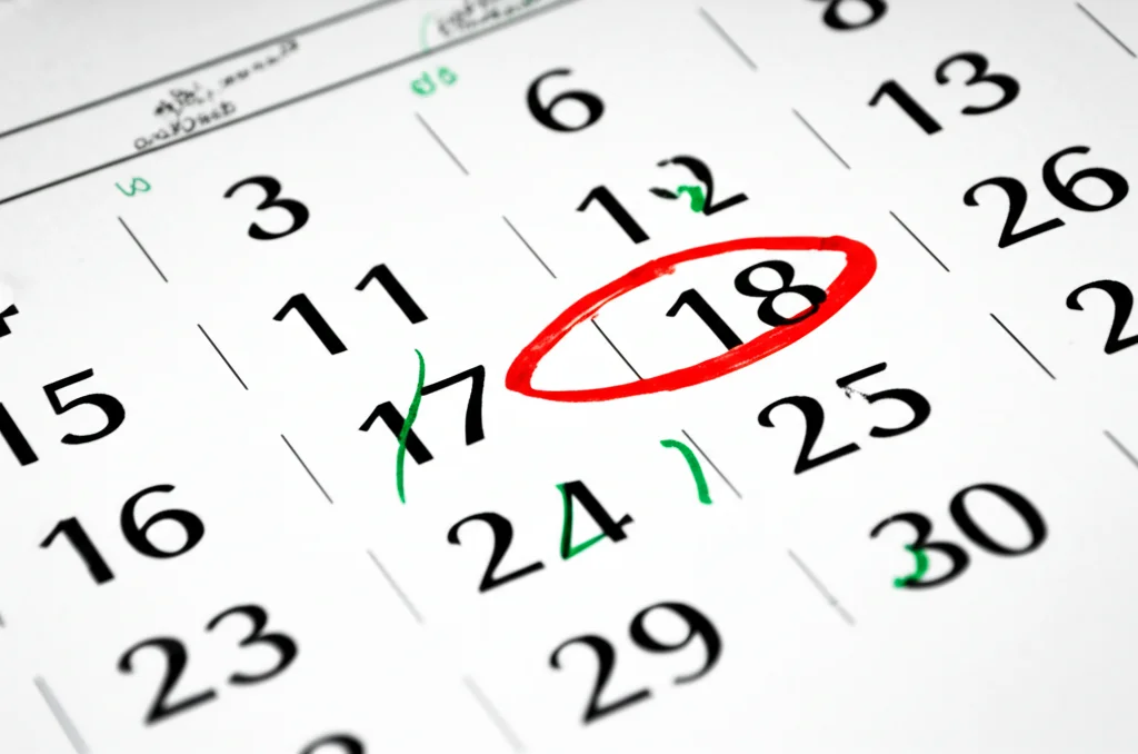 Fotografia simbolica di un calendario con i giorni segnati. Alcuni giorni sono cerchiati in rosso (ospedale) e altri in verde (casa). Obiettivo macro 100mm, alta definizione, luce controllata per evidenziare le date, focus preciso sul mese successivo a un ipotetico intervento.