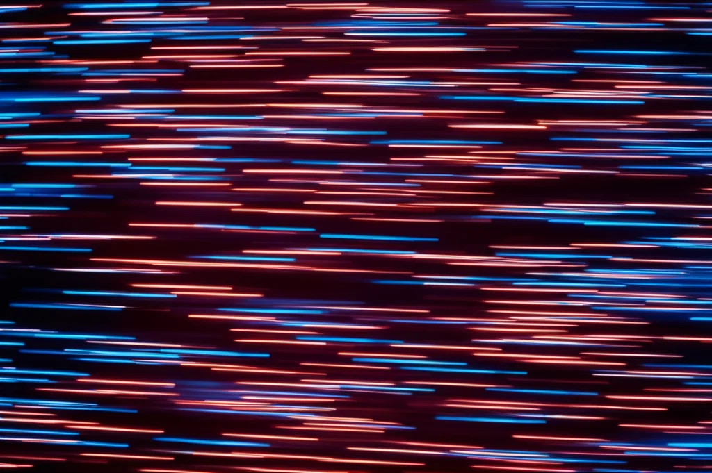 Fotografia macro di uno sciame di particelle digitali rosse e blu che formano bande parallele in movimento su uno sfondo scuro, simulando il flocking parallelo ad alta densità (HDPF). Obiettivo macro 100mm, alta definizione, illuminazione controllata per evidenziare le traiettorie dense e parallele.