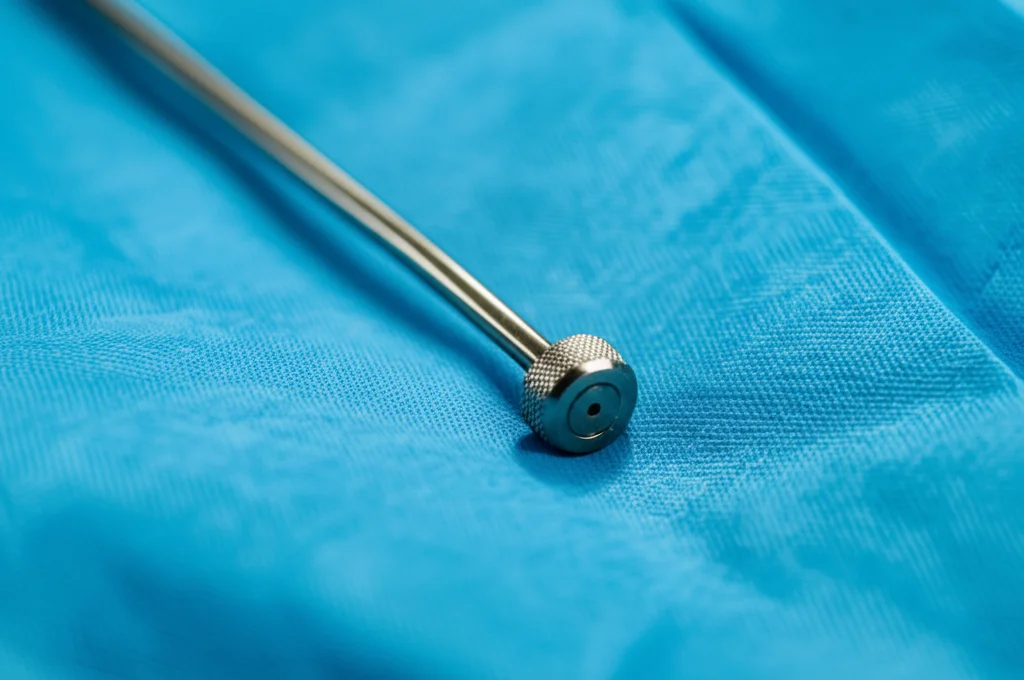 Fotografia macro di uno strumento chirurgico laparoscopico metallico lucido appoggiato su un telo chirurgico blu sterile, illuminazione controllata da studio, obiettivo macro 100mm, alta definizione, messa a fuoco precisa sullo strumento.