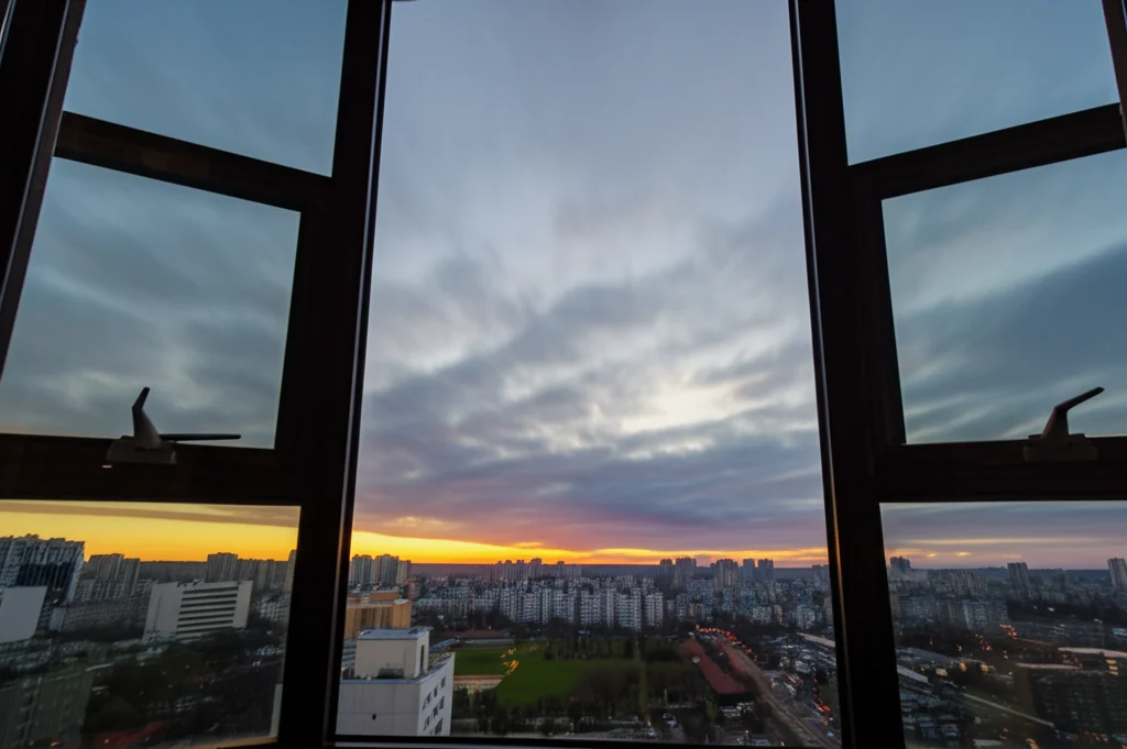 Paesaggio grandangolare di un'alba luminosa su una città tranquilla, vista da una finestra, simboleggiando speranza e un nuovo inizio. Obiettivo grandangolare 10-24mm, lunga esposizione per nuvole soffici, messa a fuoco nitida sull'orizzonte.