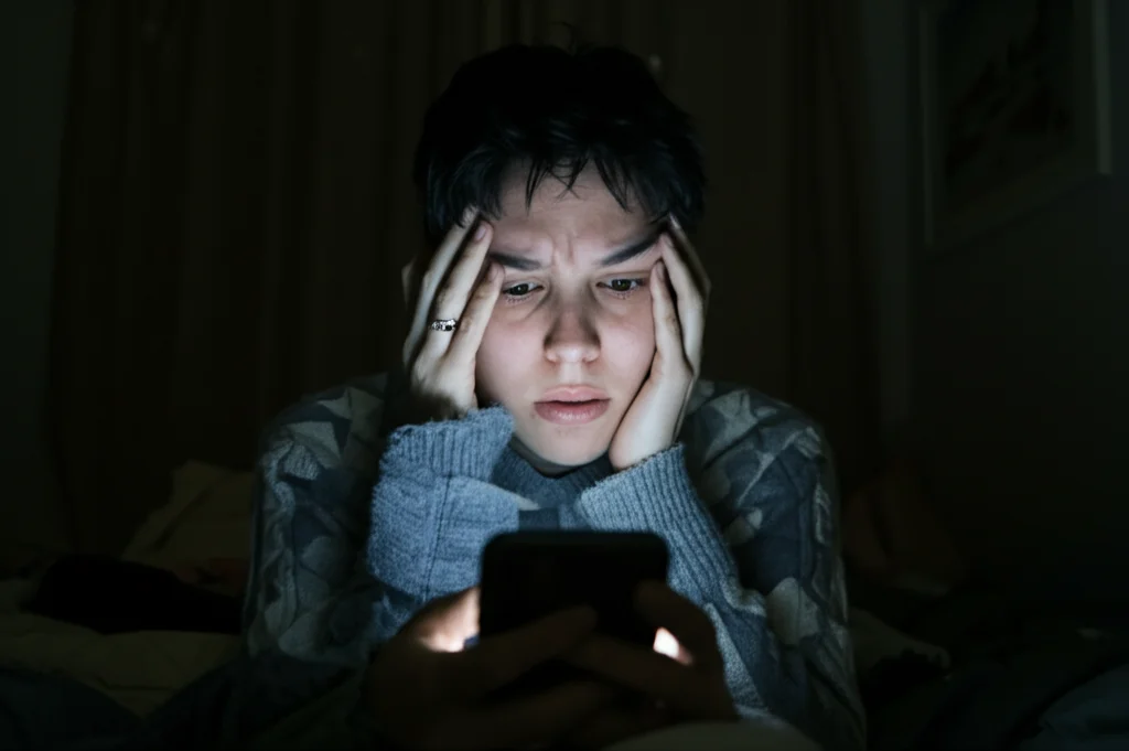 Ritratto di una persona con espressione ansiosa illuminata dalla luce bluastra di uno smartphone in una stanza buia, 35mm portrait, depth of field, duotone blu e nero