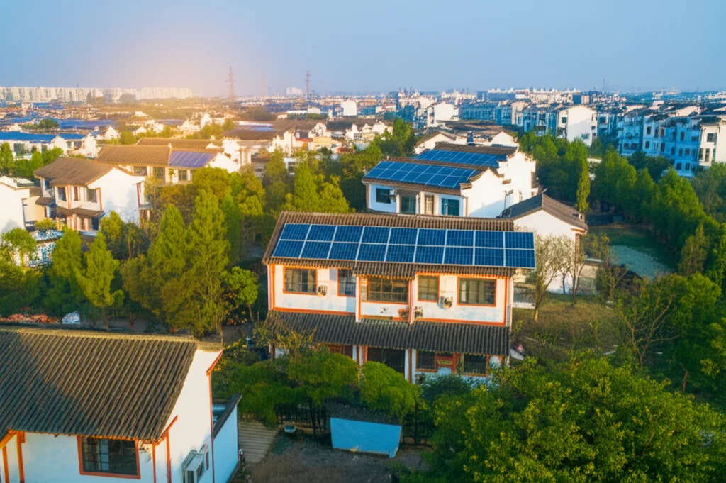 Veduta aerea di un'area suburbana cinese nella provincia di Jiangsu, con un mix di case tradizionali e moderne immerse nel verde, alcune con tetti dotati di pannelli solari. Fotografia paesaggistica, obiettivo grandangolare 20mm, luce naturale del tardo pomeriggio, alta definizione, atmosfera serena.