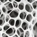 Fotografia macro ad altissima definizione di uno scaffold osseo innovativo basato su Voronoi, con trabecole orientate in modo controllato. Obiettivo macro 90mm, illuminazione da studio controllata per esaltare la microstruttura tridimensionale e la porosità ottimizzata per la rigenerazione ossea. Materiale biocompatibile bianco traslucido.