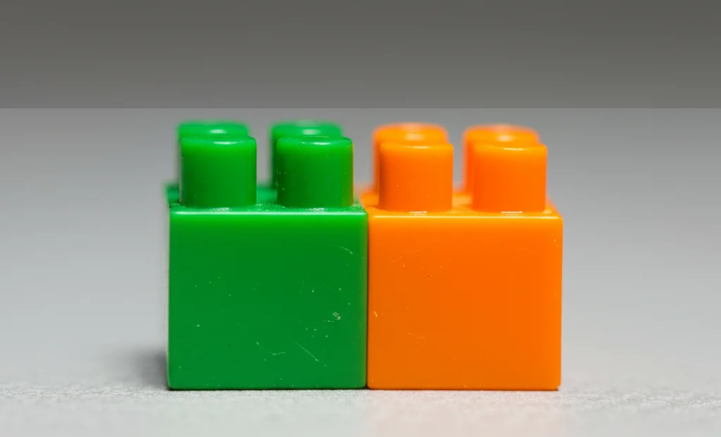 Fotografia macro realistica di due blocchi giocattolo colorati, uno leggermente più grande dell'altro, su uno sfondo neutro e sfocato. Obiettivo macro 90mm, illuminazione controllata per evidenziare le texture, messa a fuoco precisa sui blocchi.