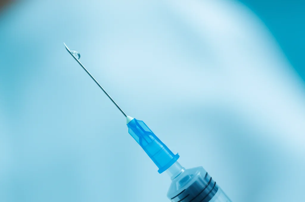 Dettaglio macro di una siringa e una provetta utilizzate per l'amniocentesi in un ambiente clinico sterile e luminoso, obiettivo macro 100mm, messa a fuoco estremamente precisa sulla punta della siringa, alta definizione dei dettagli.