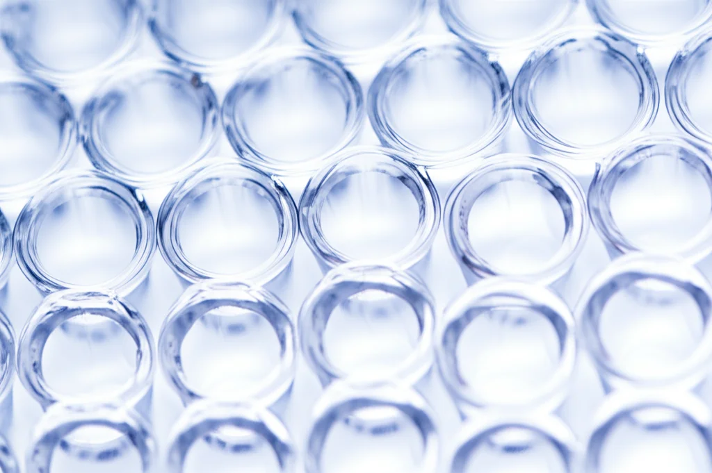 Primo piano di una piastra multi-pozzetto utilizzata per l'analisi proteomica in un laboratorio di ricerca sul cancro. Obiettivo macro 100mm, illuminazione controllata da laboratorio, alta risoluzione dei dettagli delle gocce di liquido nei pozzetti, focus preciso sui campioni.