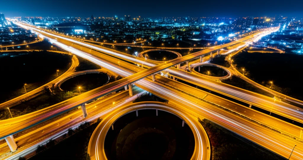 Fotografia aerea, stile paesaggistico, di una complessa rete di autostrade illuminate di notte che si intersecano vicino a un'area urbana, obiettivo grandangolare 14mm, lunga esposizione per creare scie luminose dalle auto, messa a fuoco nitida su tutta la scena, colori vibranti delle luci.