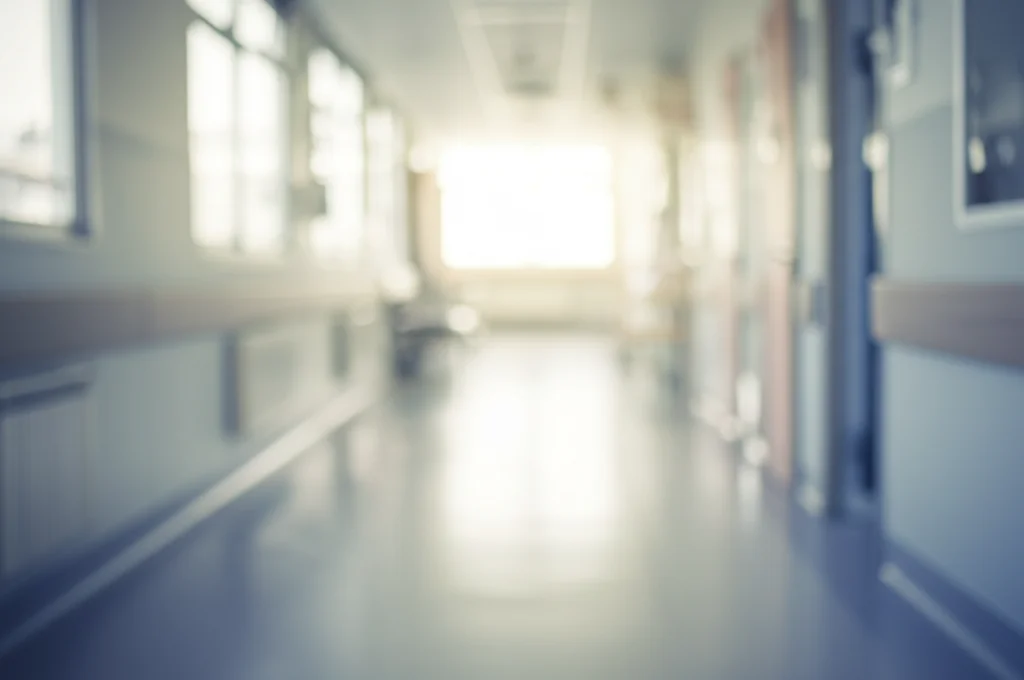 Fotografia di un corridoio d'ospedale pediatrico luminoso ma vuoto, visto da un angolo basso, obiettivo 24mm, profondità di campo che sfoca leggermente lo sfondo, luce naturale soffusa dalle finestre, evocando un senso di quiete ma anche la complessità invisibile delle vite dei pazienti. Colori tenui.