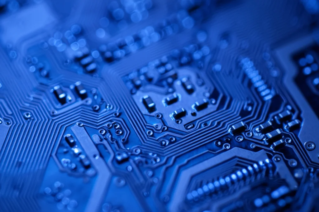 Primo piano macro di un microchip complesso illuminato da una luce bluastra fredda, che simboleggia i primi algoritmi evolutivi. Obiettivo macro 90mm, alta definizione, illuminazione controllata per evidenziare i dettagli intricati dei circuiti.