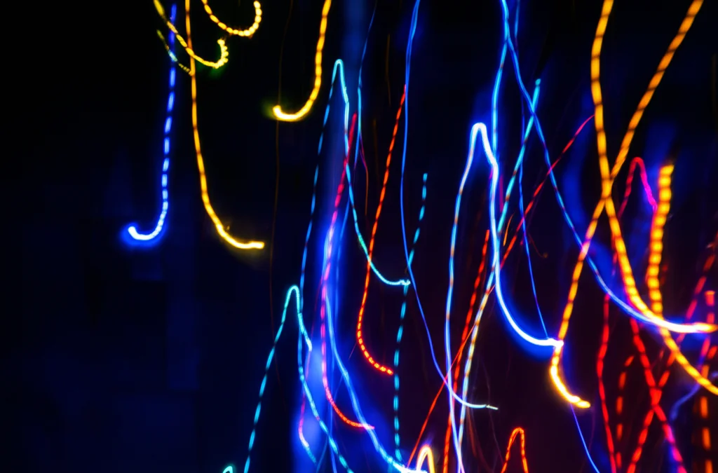 Visualizzazione artistica astratta di forme di vita digitali simili a meduse che fluttuano in un cyberspazio scuro, con colori neon vibranti. Obiettivo grandangolare 20mm, lunga esposizione per creare scie luminose fluide, evocando la simulazione della vita artificiale.