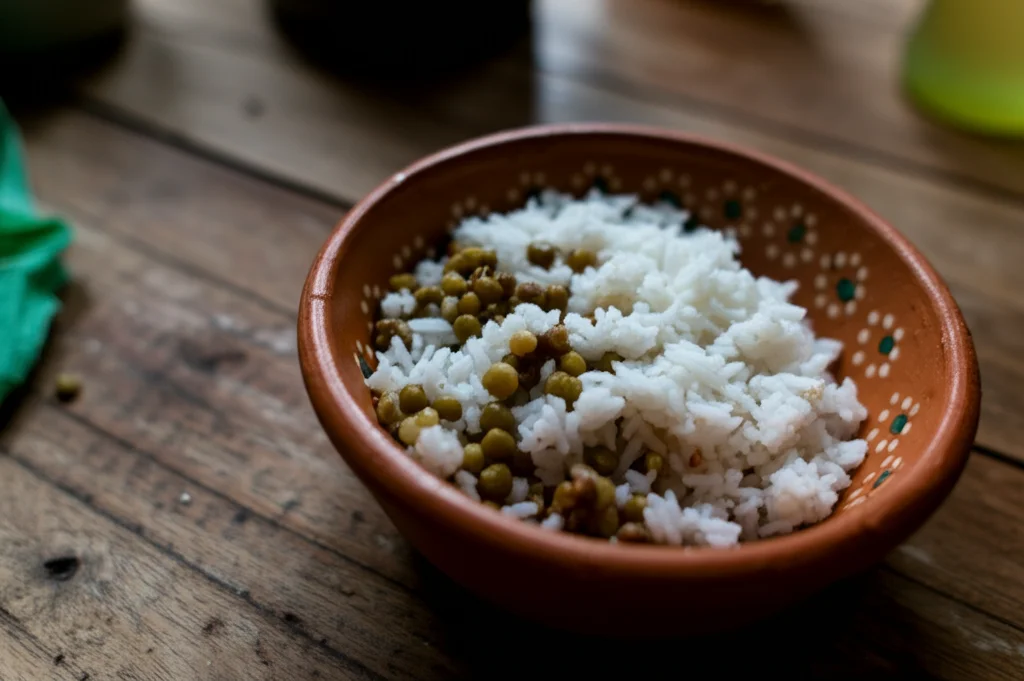 Fotografia macro di una ciotola di cibo semplice, come riso e legumi, su un tavolo di legno grezzo in una casa umile colombiana. Luce controllata che evidenzia la scarsità ma anche la dignità del pasto. Obiettivo macro 100mm, alta definizione, messa a fuoco precisa.