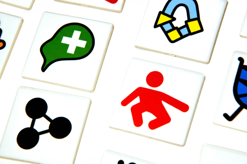 Fotografia macro di simboli visivi colorati usati per la comunicazione alternativa (come quelli di TalkingMats), obiettivo macro 90mm, alta definizione dei dettagli, luce da studio controllata e diffusa per minimizzare le ombre.