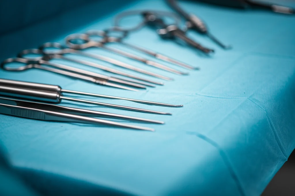 Primo piano macro di strumenti chirurgici laparoscopici sterilizzati su un telo blu sterile in sala operatoria, illuminazione chirurgica controllata e brillante, messa a fuoco precisa sulla punta degli strumenti, 100mm Macro lens, high detail.