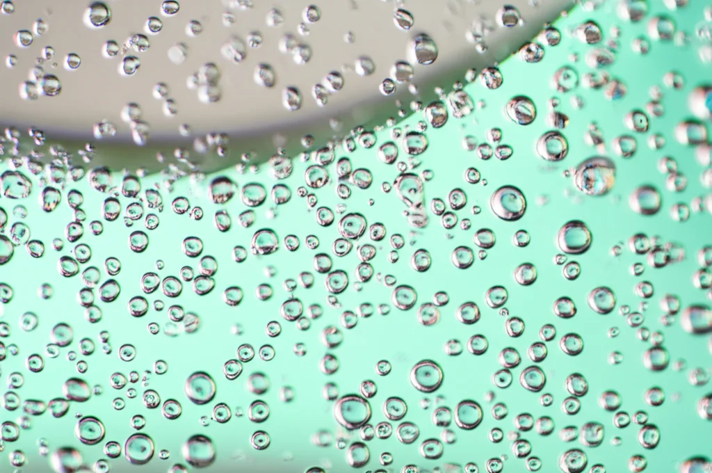 Macro fotografia di goccioline lattiginose di nanoemulsione di olio di rosmarino in acqua, obiettivo macro 100mm, alta definizione, illuminazione controllata che evidenzia la dispersione fine delle particelle.