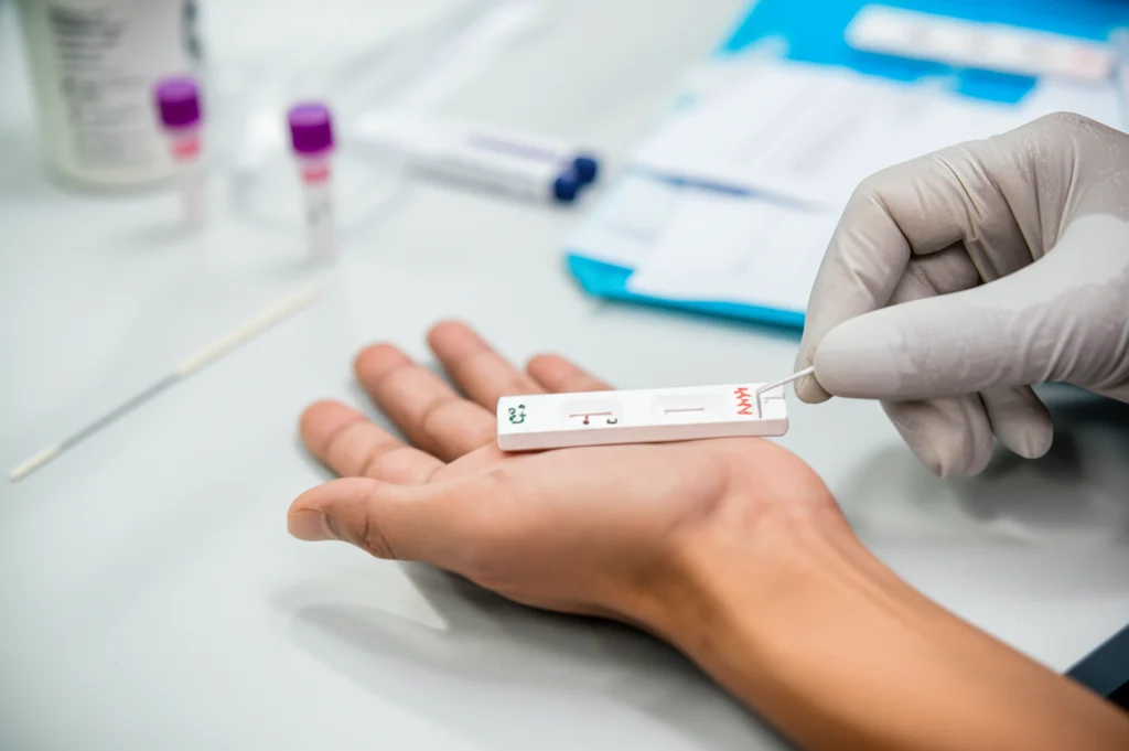 Fotografia di una mano guantata di un operatore sanitario che esegue un test rapido diagnostico per HIV o HCV su un campione di sangue, ambientazione clinica, obiettivo macro 60mm, alta definizione sui dettagli del test kit.