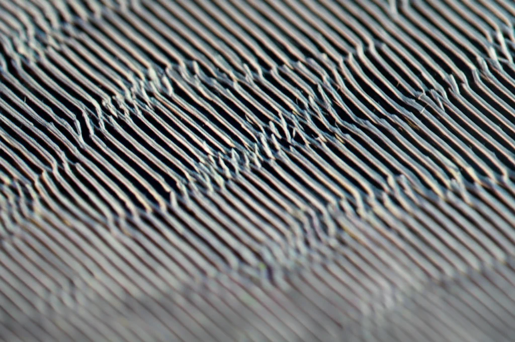 Primo piano macro di una metalente nanofabbricata su substrato di vetro, illuminata da un fascio laser focalizzato. Si vedono chiaramente le nanostrutture periodiche (nanopilastri). Dettaglio elevato, messa a fuoco precisa, illuminazione controllata da laboratorio, obiettivo macro 100mm.