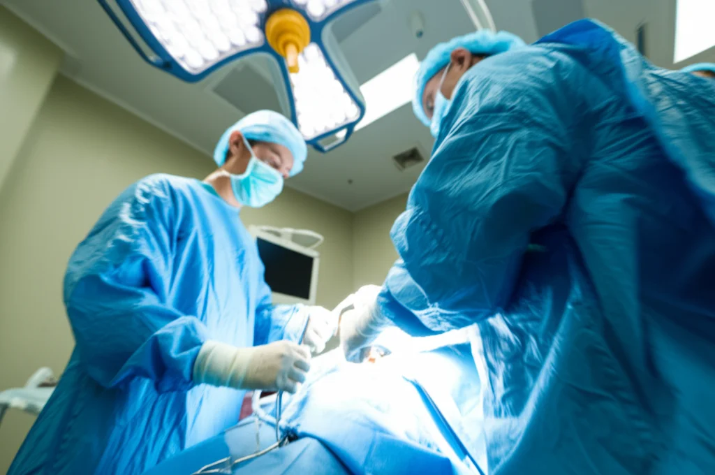 Scatto grandangolare, obiettivo da 24 mm, all'interno di una moderna sala operatoria durante la chirurgia del ginocchio, concentrarsi sul team chirurgico che lavora sotto luci intense, trasmettendo complessità e sfida. Leggero movimento del movimento sulle mani per indicare l'attività. Il team Chirurgico al Lavoro Dorente Un intervento Complice Al Ginocchio.