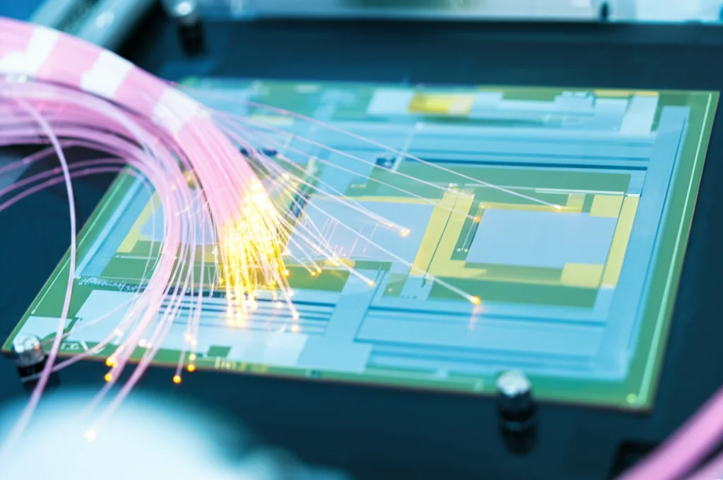 Immagine fotorealistica di un chip fotonico in silicio su un banco di laboratorio, collegato da fibre ottiche, con sottili percorsi di luce luminosa visibili all'interno della struttura del chip, obiettivo macro, 70mm, alto dettaglio, messa a fuoco precisa, illuminazione controllata da laboratorio.