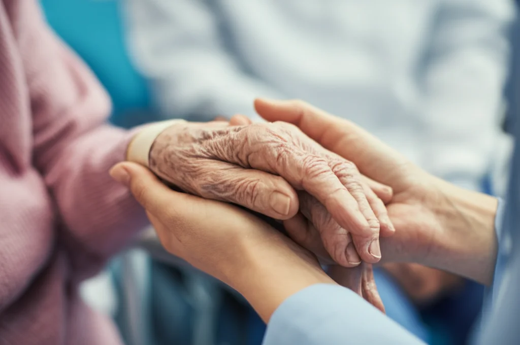 Scatto ravvicinato, due paia di mani strette delicatamente, una più anziana e fragile, l'altra più giovane e solidale, illuminazione interna morbida, lenti macro, 85 mm, dettagli elevati, trasmettendo empatia e connessione in un ambiente sanitario.