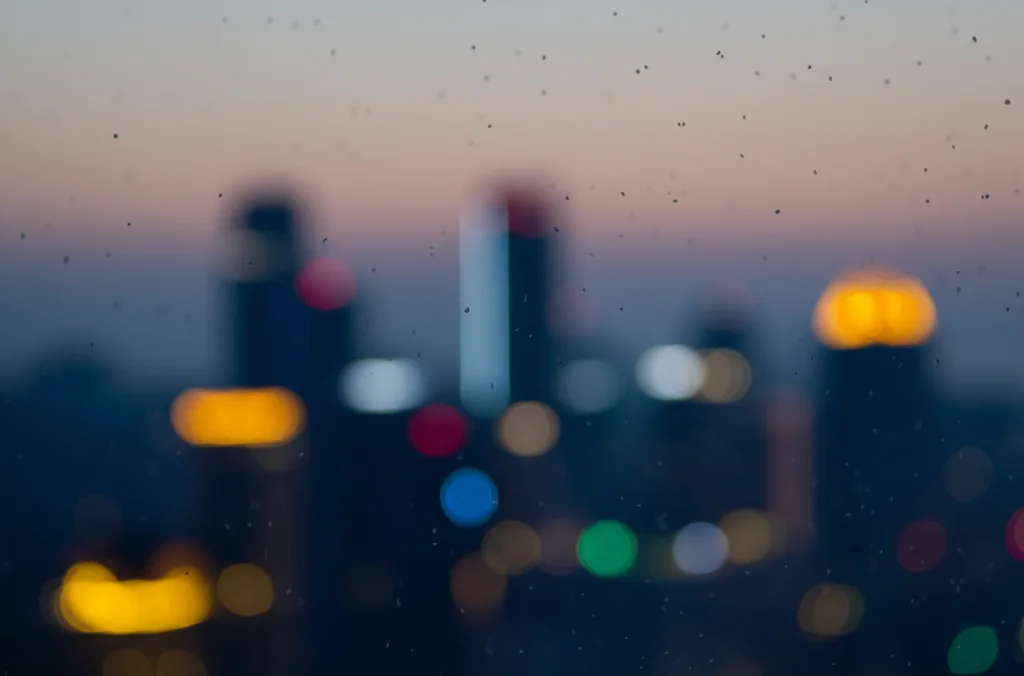 Fotografia macro di particelle di PM2.5 sospese nell'aria sopra uno skyline urbano cinese sfocato al tramonto, illuminazione controllata, alta definizione, lente macro 100mm, messa a fuoco precisa.