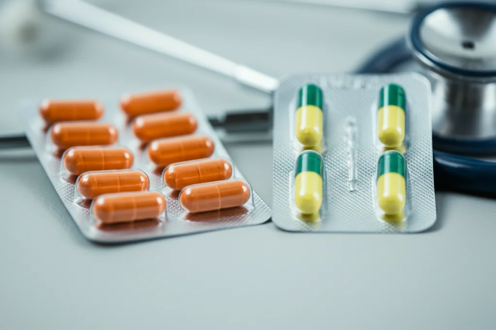 Primo piano di capsule di farmaci ARNi (sacubitril/valsartan) accanto a un blister di ACE-inibitori su un tavolo medico pulito, profondità di campo ridotta, illuminazione da studio morbida, obiettivo prime 50mm.