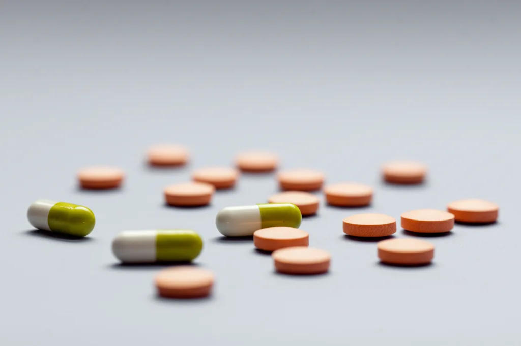 Fotografia di diverse pillole di corticosteroidi sparse su un tavolo, obiettivo macro 60mm, alta definizione, messa a fuoco precisa su una pillola, luce soffusa, simboleggiando la dipendenza e la necessità di ridurre l'uso di steroidi nel lupus.