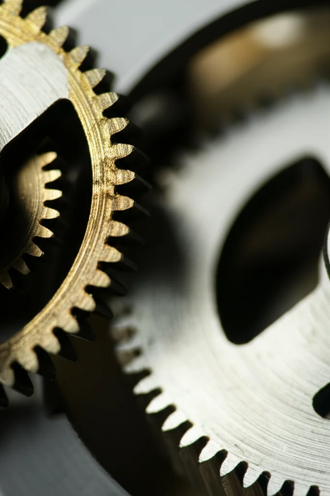 Fotografia macro di ingranaggi metallici complessi e interconnessi, alcuni leggermente sfocati per indicare movimento o cambiamento. Obiettivo macro 100mm, illuminazione controllata per evidenziare i dettagli e le texture metalliche, alta definizione.