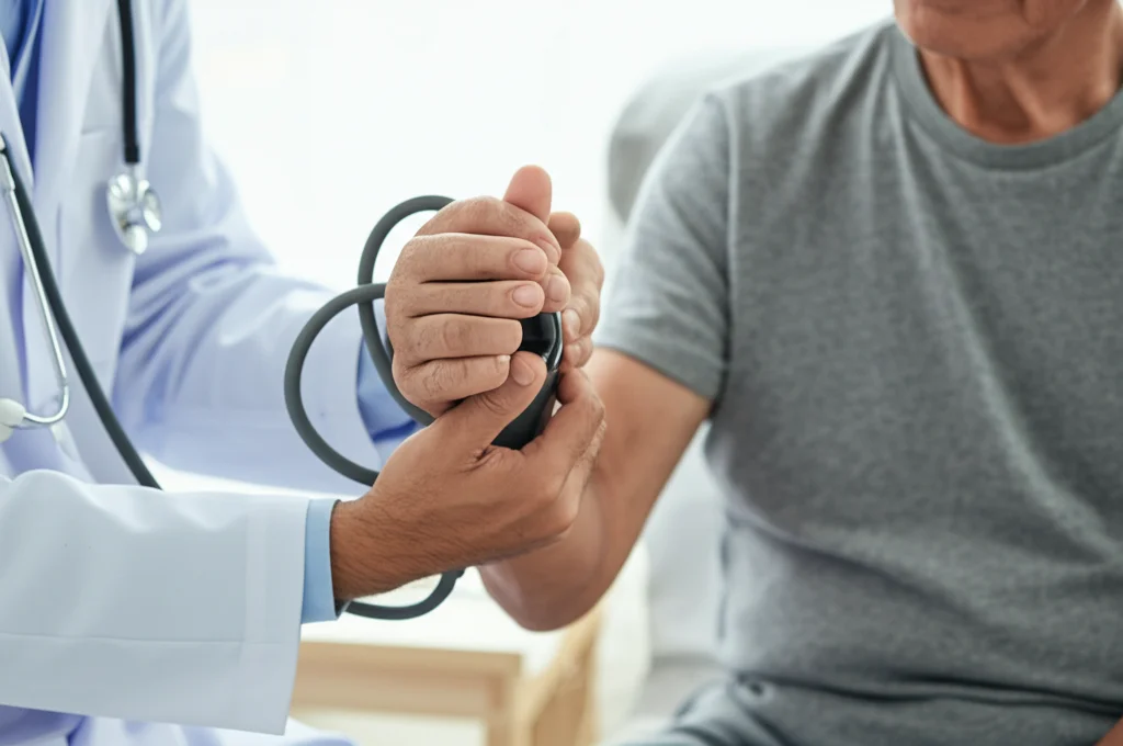 Fotografia realistica di un medico che esegue un test di forza della presa della mano (handgrip strength) su un paziente anziano in un ambiente clinico luminoso. Si vede il dinamometro nella mano del paziente e il medico che osserva. Obiettivo prime, 35mm, profondità di campo che sfoca leggermente lo sfondo, illuminazione controllata.