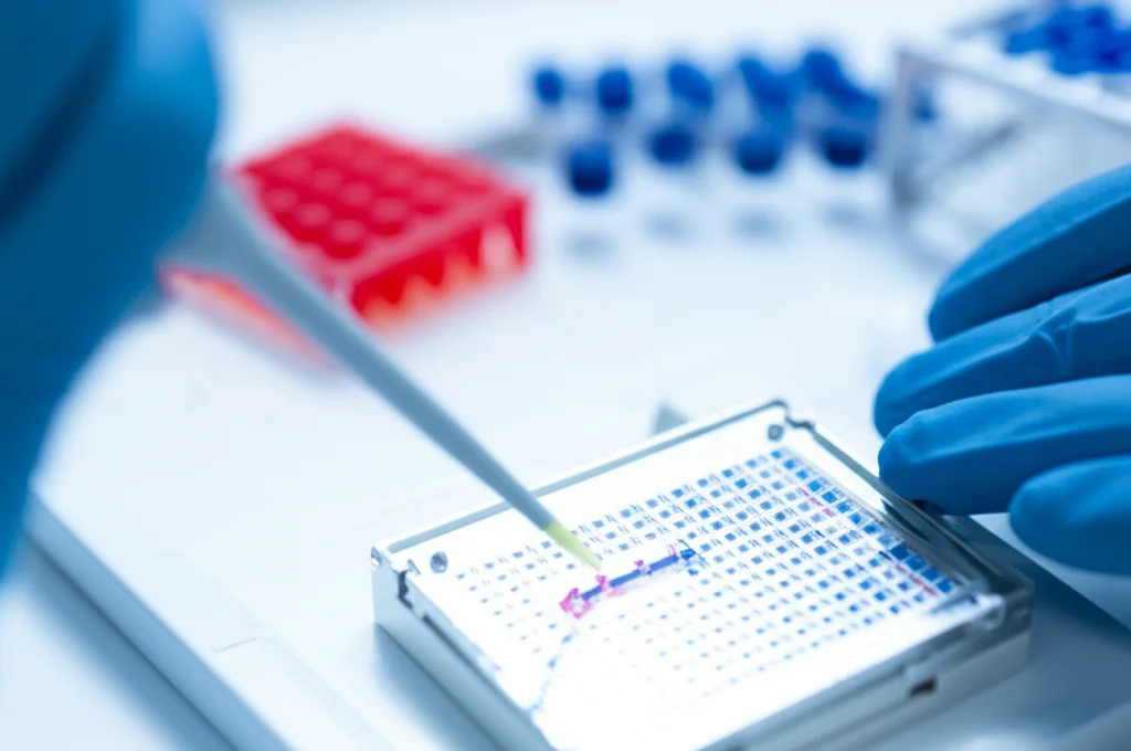 Fotografia realistica di un tecnico di laboratorio che carica un campione di DNA su un chip per analisi di metilazione (come un chip Illumina EPIC). Dettaglio sulle mani guantate, sulla pipetta e sul chip. Illuminazione da laboratorio brillante ma focalizzata sull'azione. Obiettivo prime 50mm, profondità di campo ridotta.