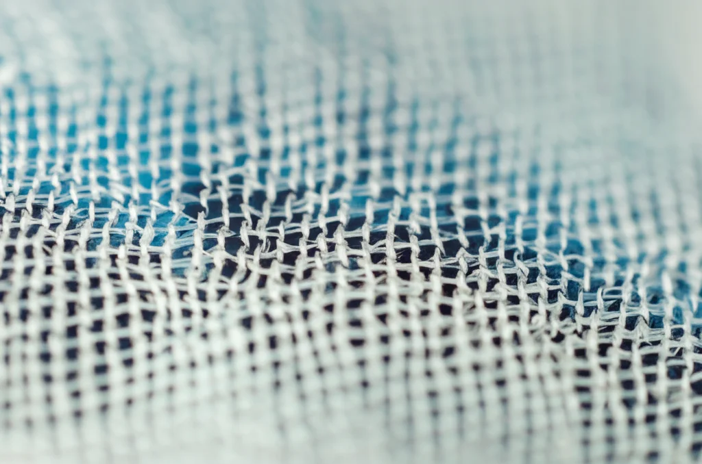 Primo piano macro di una rete chirurgica sintetica (polipropilene) simile a uno sling mid-uretrale, illuminazione controllata, alta definizione, obiettivo macro 100mm, per illustrare il materiale usato e la potenziale causa dell'erosione.