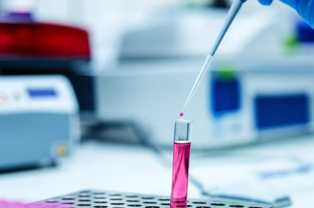 Fotografia di laboratorio, obiettivo macro 60mm, che mostra una pipetta che rilascia un campione di DNA in una provetta per il sequenziamento genetico (NGS), con apparecchiature scientifiche sfocate sullo sfondo, illuminazione precisa e alta definizione.