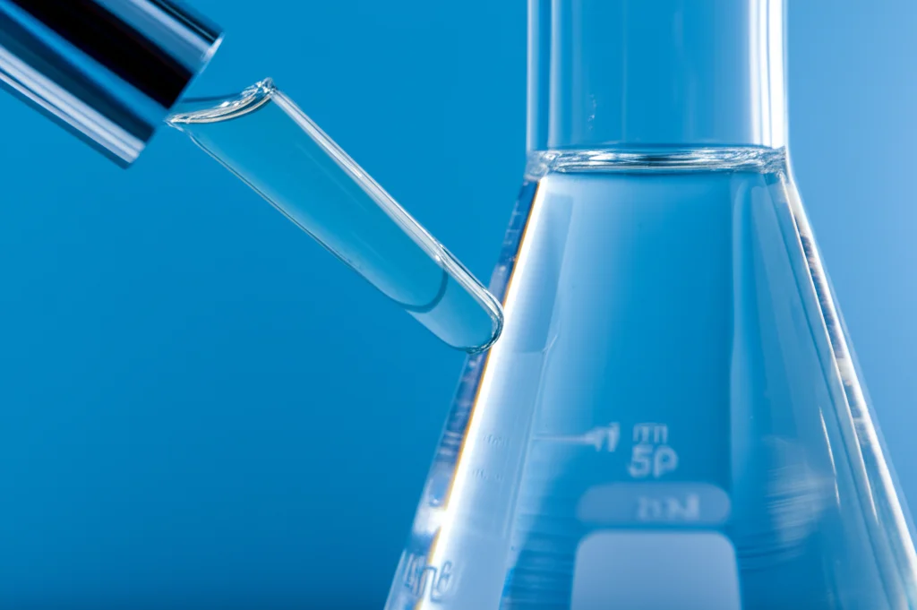 Immagine macro di un liquido ionico trasparente e leggermente viscoso contenuto in una beuta da laboratorio, illuminazione laterale controllata che ne esalta la purezza, obiettivo macro 100mm, alta definizione dei dettagli.