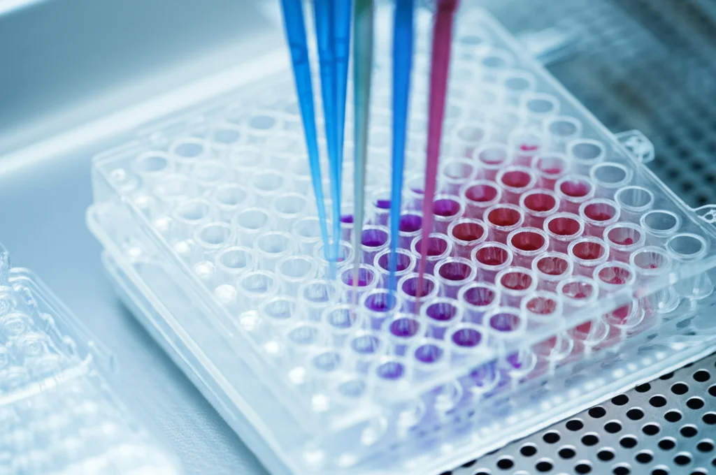 Primo piano di una piastra multiwell per PCR in un moderno laboratorio di diagnostica veterinaria, luce controllata e brillante sui pozzetti, obiettivo macro 100mm, alta definizione dei dettagli delle pipette e dei liquidi colorati.