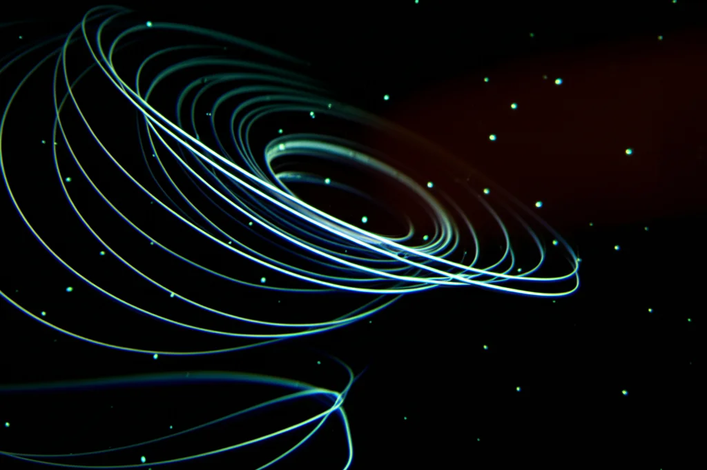 Primo piano di un anello di vortice elicoidale che ruota lentamente in un fluido scuro, visualizzato con particelle traccianti luminose. Obiettivo macro 100mm, alta definizione, messa a fuoco precisa sulla struttura elicoidale, illuminazione drammatica laterale che evidenzia la torsione.