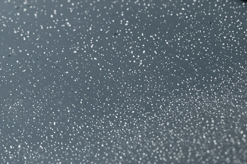 Immagine macro fotorealistica di un film sottile bilayer ZnO/TiO2 depositato su un substrato di vetro. Si notano particelle sferiche fini sulla superficie. Obiettivo macro 100mm, alta definizione, illuminazione controllata per evidenziare la texture superficiale.