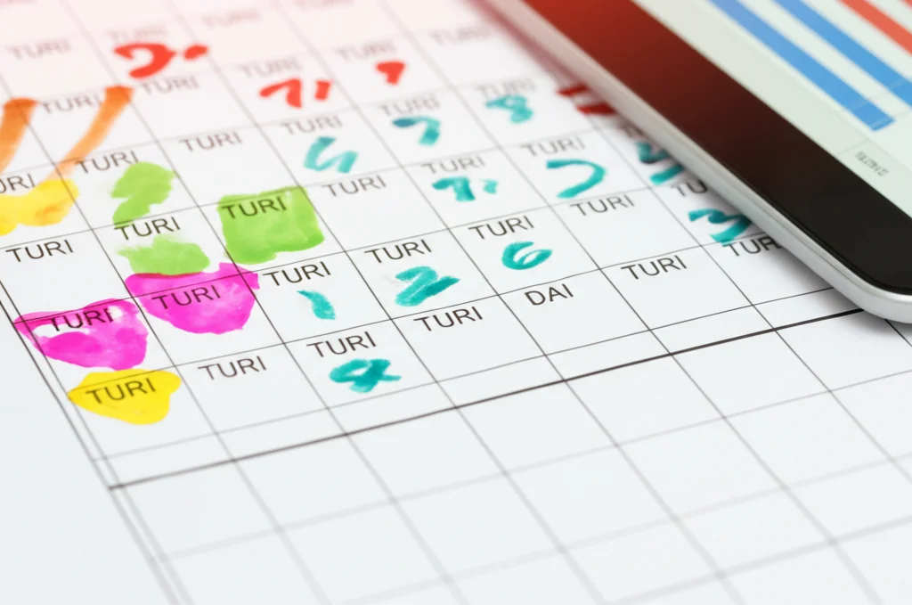 Foto macro di un planning cartaceo con evidenziati turni di lavoro per l'assistenza domiciliare, accanto a un tablet che mostra un software di pianificazione. Obiettivo macro 80mm, alta definizione, focus preciso sui dettagli del planning.