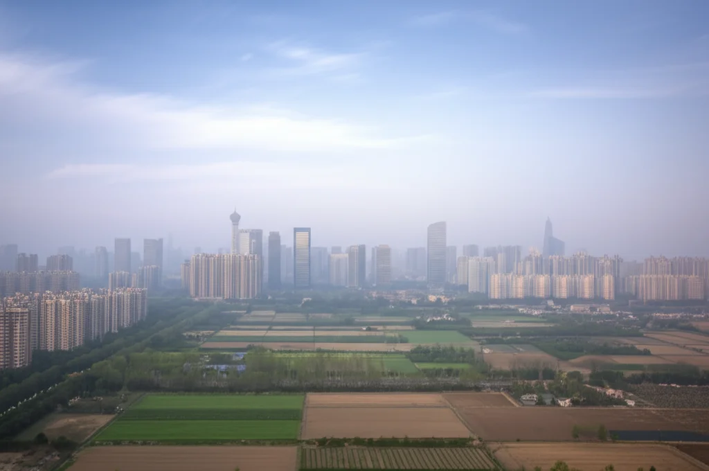 Scatto grandangolare 20mm che mostra il contrasto tra un orizzonte urbano cinese moderno ma avvolto nello smog e un paesaggio rurale adiacente con campi coltivati sotto un cielo leggermente più limpido. Lungo tempo di esposizione per accentuare la foschia urbana.