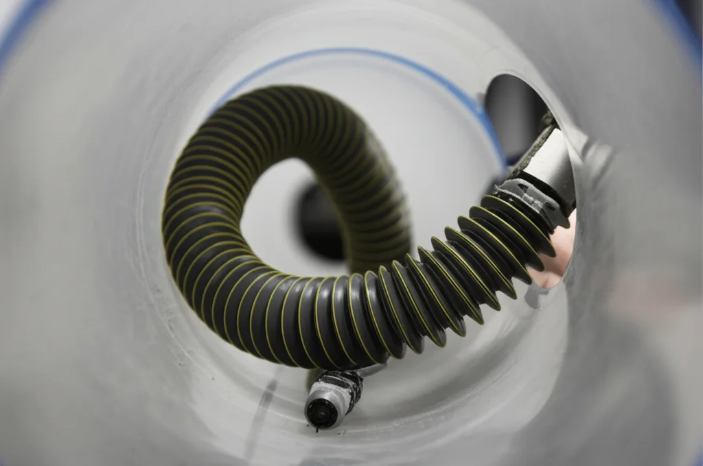 Scatto grandangolare, obiettivo 20mm, messa a fuoco nitida, che cattura il robot morbido ispirato ai serpenti (ICSBot) mentre naviga all'interno di uno stretto tubo trasparente a forma di S, simulando la locomozione a fisarmonica in un ambiente confinato e complesso.