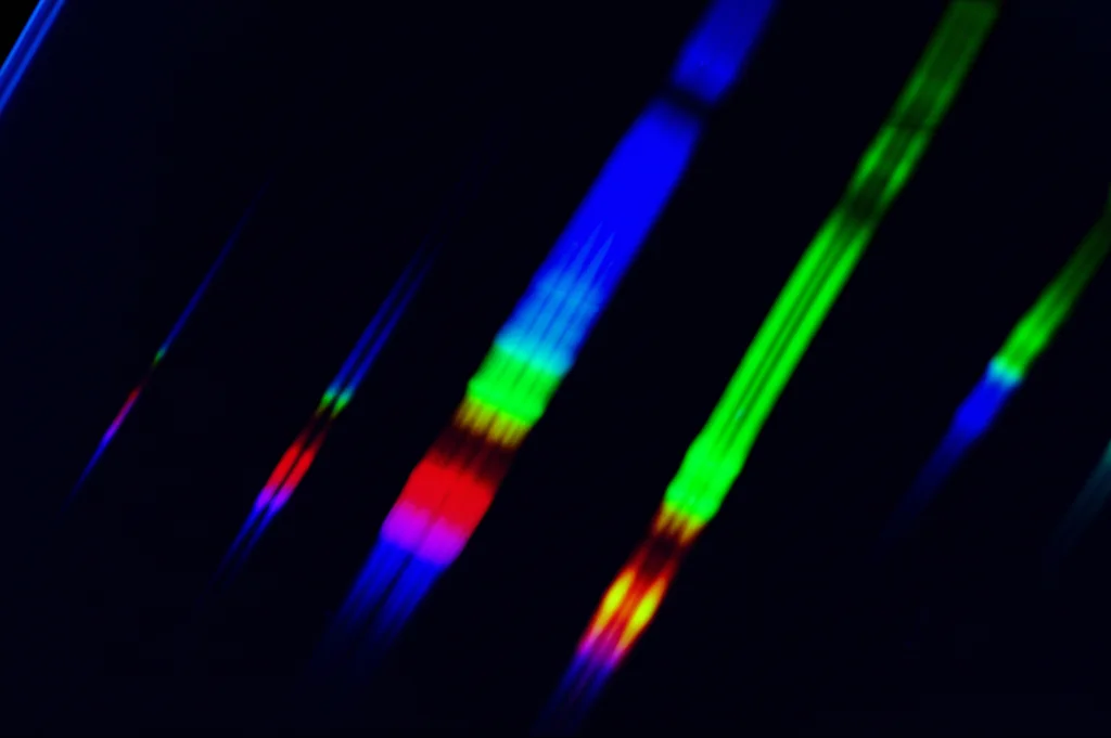 Immagine macro ad alta definizione di una lastra HPTLC illuminata da luce UV 366nm, che mostra bande fluorescenti colorate separate. Lente macro 100mm, illuminazione controllata per evidenziare i dettagli delle bande chimiche della formula medicinale tailandese Ya-Kao.