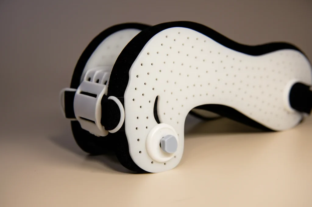 Fotografia still life di un'ortesi pelvica DEFO appoggiata su una superficie neutra. Obiettivo macro 90mm, alta definizione dei dettagli del tessuto elastomerico, illuminazione controllata per evidenziare la texture. Stile fotorealistico.