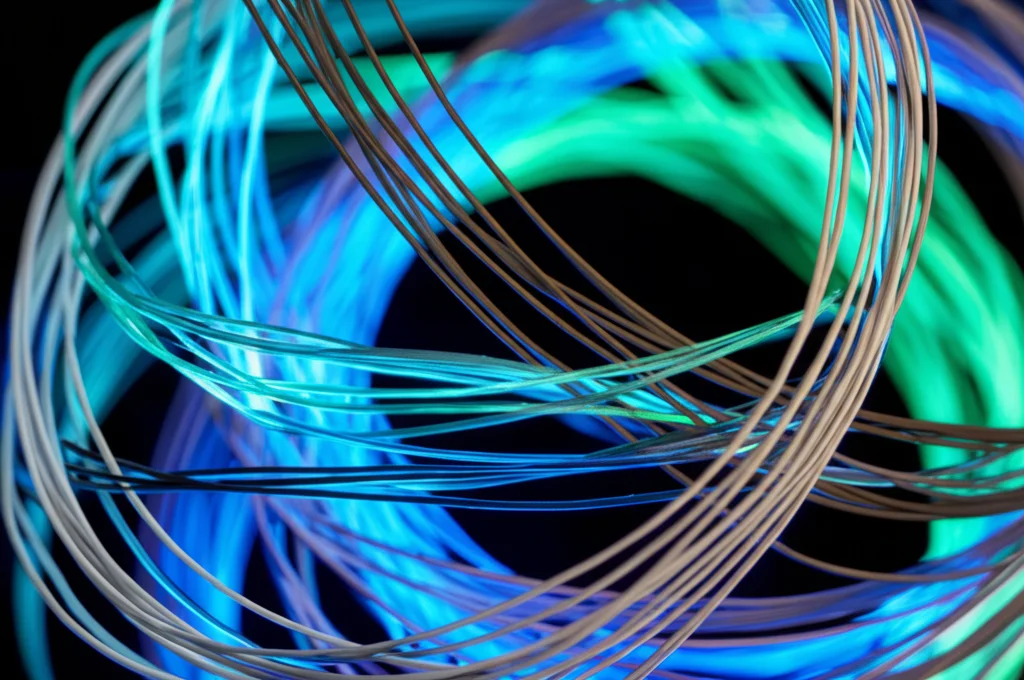 Fotografia macro ad alta definizione di una complessa struttura a spirale simile al DNA, realizzata con filamenti luminosi di colori diversi (blu, verde, grigio) che si intrecciano, simboleggiando l'interazione dinamica e la selezione nel modello della Tripla Elica. Obiettivo macro 100mm, messa a fuoco precisa sui punti di intersezione, sfondo scuro per esaltare la luminosità.