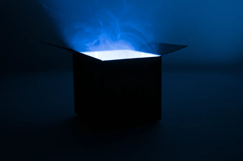 Fotografia astratta di una scatola nera semiaperta da cui fuoriesce luce blu brillante, simboleggiando la complessità interna dell'IA. Obiettivo prime 50mm, profondità di campo ridotta per focalizzare sulla luce, sfondo scuro e minimale, illuminazione drammatica.