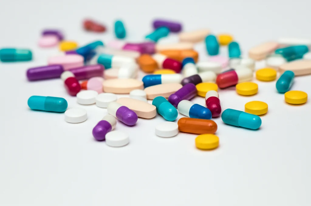 Fotografia macro di diverse pillole antibiotiche colorate sparse su una superficie bianca, luce da studio controllata, alta definizione, lente macro 60mm, focus selettivo su una pillola.
