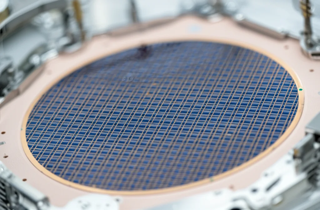 Fotografia grandangolare, lente 20mm, di un wafer di silicio da 200mm in una cleanroom high-tech, mostrando la matrice di fotorilevatori GFET-QD fabbricati su larga scala, messa a fuoco nitida sull'intera superficie del wafer.