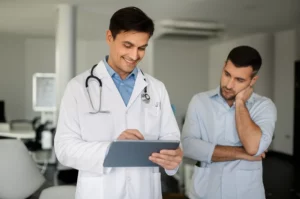 Un medico di base sorridente che discute con un paziente in uno studio medico moderno, entrambi guardano un tablet che potrebbe mostrare informazioni sul dolore al collo. Prime lens, 35mm, depth of field, luce naturale e calda.