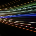 Wide-angle lens, 15mm, long exposure, sharp focus, raffigurante una rappresentazione astratta e stilizzata di un'onda epidemica che si propaga attraverso un paesaggio oscuro. Linee luminose indicano i percorsi dell'infezione, creando un senso di movimento dinamico e interconnessione globale.